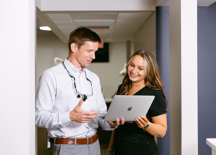 Dentist looking at laptop and smiling together with his assistant