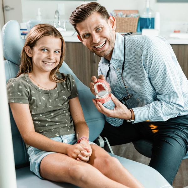 Dr. Escobar is smiling with his young patient and holding a model of braces