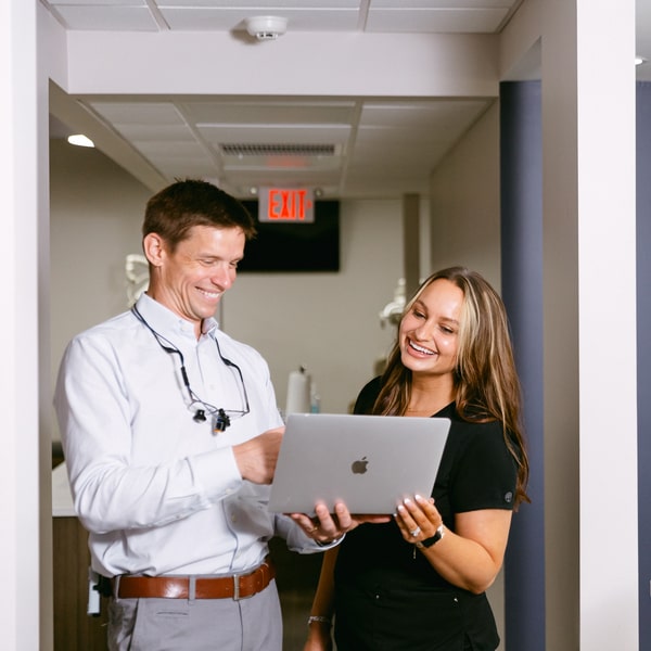 Explore the Steps to Becoming a Board-Certified Orthodontist! Dr. McEntire is happily smiling with smiling tam member holding a laptop